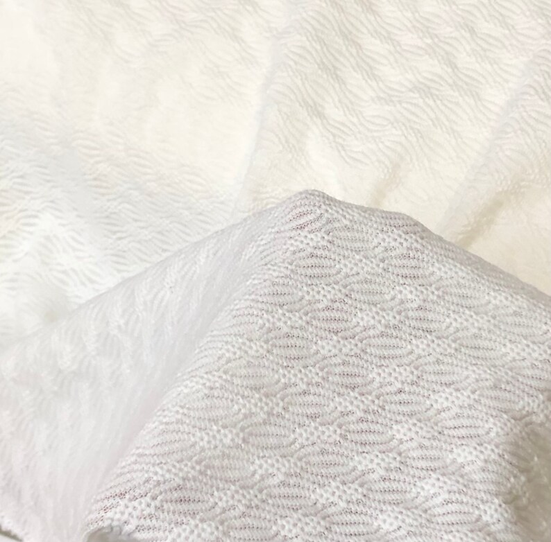 May include: White textured fabric with a woven pattern. The fabric is folded in half, showing the texture and pattern on both sides.