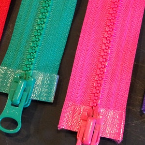 May include: Three zipper pulls in different colors: green, pink, and red. The zipper pulls are made of metal and have a loop at the top.
