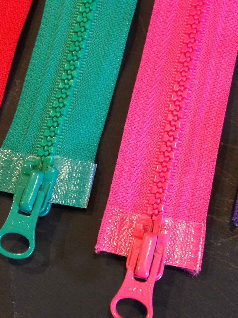 May include: Three zipper pulls in different colors: green, pink, and red. The zipper pulls are made of metal and have a loop at the top.