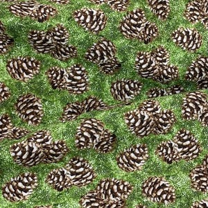 May include: A green fabric with a repeating pattern of brown pine cones. The fabric has a textured surface.
