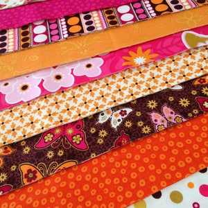 May include: A stack of colorful fabric scraps with various patterns, including polka dots, butterflies, and floral designs. The fabrics are in shades of pink, orange, brown, and white.