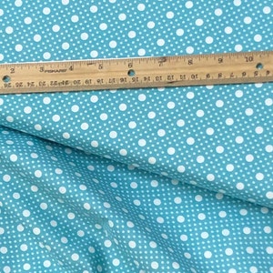 May include: A close-up of a blue fabric with a white polka dot pattern. The fabric is folded in half and a ruler is placed on top of the fabric.
