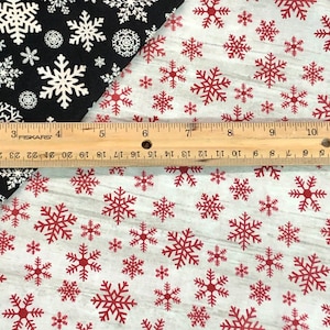 Puede incluir: Dos muestras de tela con un patrón de copo de nieve. La muestra superior es negra con copos de nieve blancos. La muestra inferior es blanca con copos de nieve rojos. Una regla se coloca entre las dos muestras.