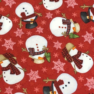 May include: Red fabric with a repeating pattern of white snowmen with black eyes and red scarves. The snowmen are holding sticks with green leaves. There are also pink snowflakes on the fabric.