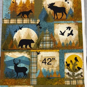 May include: Fabric panel featuring a patchwork design with woodland scenes. Each square depicts silhouettes of animals like deer, moose, and bears, along with trees and birds. The panel is 42 inches wide.