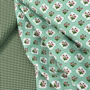 Puede incluir: Una tela verde y blanca con un patrón repetido de fresas en forma de nube. La tela está doblada por la mitad, mostrando el patrón en ambos lados.