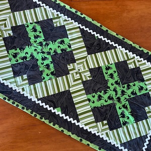 Può includere: Runner da tavolo fatto a mano con un design patchwork. Presenta tessuti neri e verdi con motivi a gatto e a righe. Il bordo bianco a zig-zag e un bordo verde con pois neri completano il design. Il runner misura circa 102 cm di lunghezza.