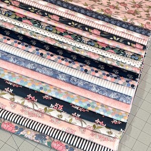 May include: A stack of various floral and patterned fabrics in shades of pink, blue, and white. The fabrics feature designs such as roses, stripes, polka dots, and geometric shapes. The fabrics are neatly stacked, showcasing a variety of textures and patterns.