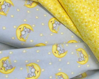 May include: Two pieces of fabric with a repeating pattern of bunnies sleeping on a crescent moon. One fabric is light blue with yellow stars and the other is yellow with white stars.