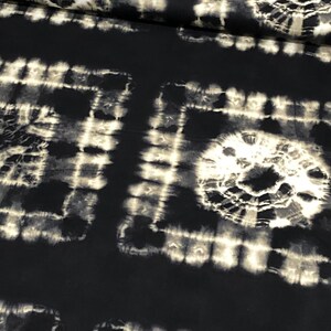 May include: Black fabric with a white tie-dye pattern. The pattern is made up of circles and squares.