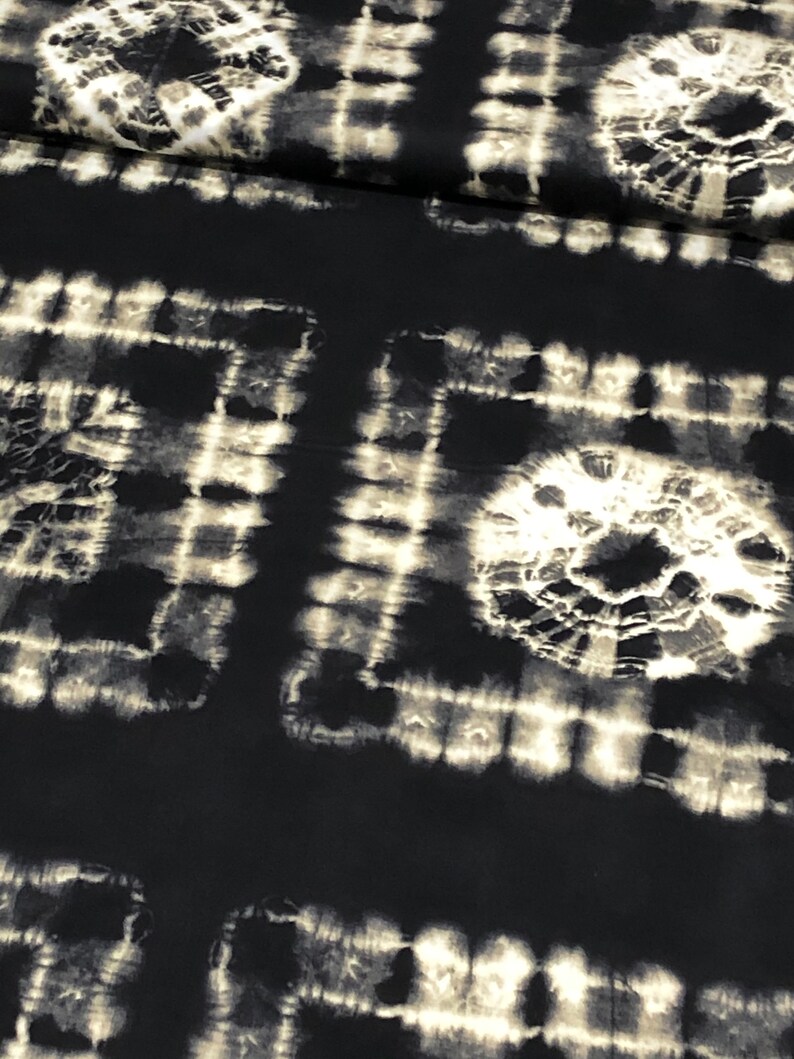 May include: Black fabric with a white tie-dye pattern. The pattern is made up of circles and squares.