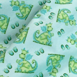 May include: A light blue fabric with a repeating pattern of green dragons and blue footprints. The dragons are cartoon-like and have wings and tails.