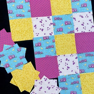 May include: A patchwork quilt in progress, featuring squares of fabric with owl and moon patterns, polka dots, and hearts. The color palette includes blue, yellow, and pink. Additional star-shaped fabric pieces are scattered around the quilt.