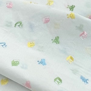May include: White fabric with a repeating pattern of colourful toy blocks and animals. The fabric has a subtle sheen and a soft texture.