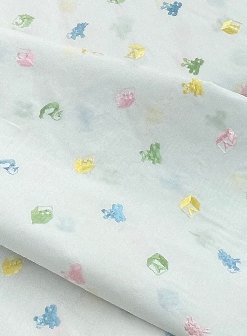 May include: White fabric with a repeating pattern of colourful toy blocks and animals. The fabric has a subtle sheen and a soft texture.