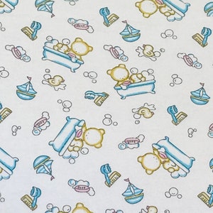 May include: A white fabric with a repeating pattern of yellow bears in a blue bathtub with white bubbles, blue sailboats, yellow ducks, and pink soap bars. The background is white.