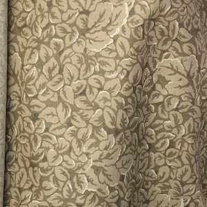 May include: A beige fabric with a white floral pattern. The fabric has a subtle texture and a soft, muted color.