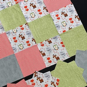 May include: A collection of fabric squares with various woodland animal prints, including owls, deer, raccoons, and foxes. The squares are in shades of red, green, and gray, and some have a checkered pattern.