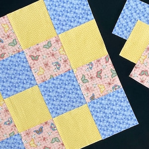 以下が含まれることがあります： 黄色、青、ピンクの布の正方形でチェッカーボードパターンになっているパッチワークキルトブロック。正方形は、小さな白いドット、蝶、グリッドパターンで飾られています。