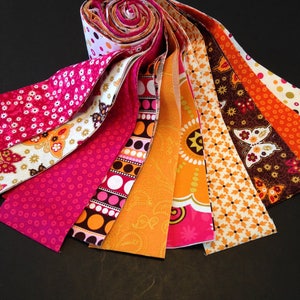 May include: A bundle of fabric strips in various shades of pink, orange, and brown with different patterns, including polka dots, paisley, and floral designs.