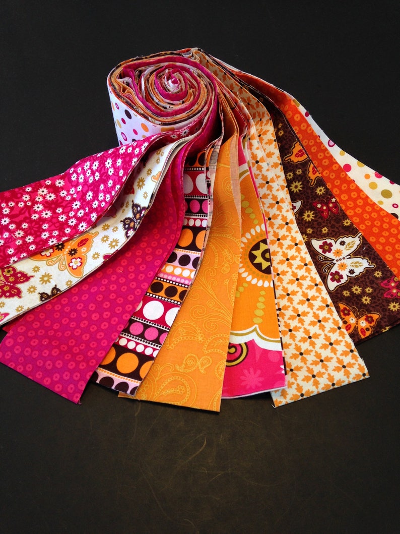 May include: A bundle of fabric strips in various shades of pink, orange, and brown with different patterns, including polka dots, paisley, and floral designs.