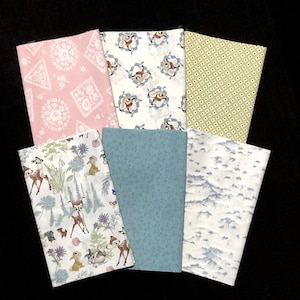May include: A set of six fabric squares featuring a variety of patterns, including a pink floral design, a white background with a repeating deer pattern, a green and white geometric pattern, a blue floral pattern, a white background with a repeating deer pattern, and a white background with a light blue cloud pattern.