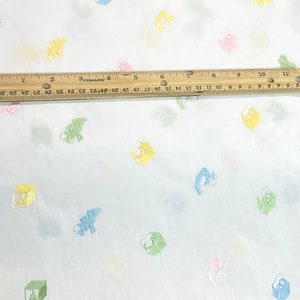 May include: White fabric with a repeating pattern of colourful embroidered blocks and animals. The blocks are in shades of green, yellow, blue, and pink. The animals are a light blue fish, a green dinosaur, and a pink bunny.