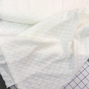 May include: White fabric with a textured, woven pattern. The fabric has a subtle sheen and a soft, drapey feel.