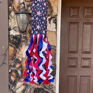 May include: A red, white, and blue windsock with a black background and white stars. The windsock is hanging from a hook on a stone wall.