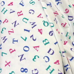 Könnte beinhalten: Weißer Stoff mit einem sich wiederholenden Muster aus bunten Buchstaben und Zahlen. Die Buchstaben sind in Rosa, Blau, Grün und Lila. Die Zahlen sind in Rosa, Blau und Grün.