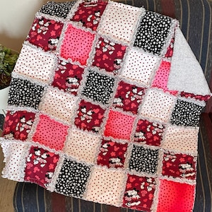 May include: A red, pink, black and white patchwork quilt with a Mickey Mouse and Minnie Mouse design. The quilt is made of squares of different fabrics and has a frayed edge.