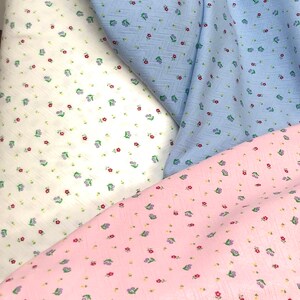 K&ouml;nnte beinhalten: Drei Stoffmuster mit einem kleinen Blumenmuster. Die Muster sind wei&szlig; mit roten Blumen, hellblau mit roten Blumen und rosa mit lila und roten Blumen.