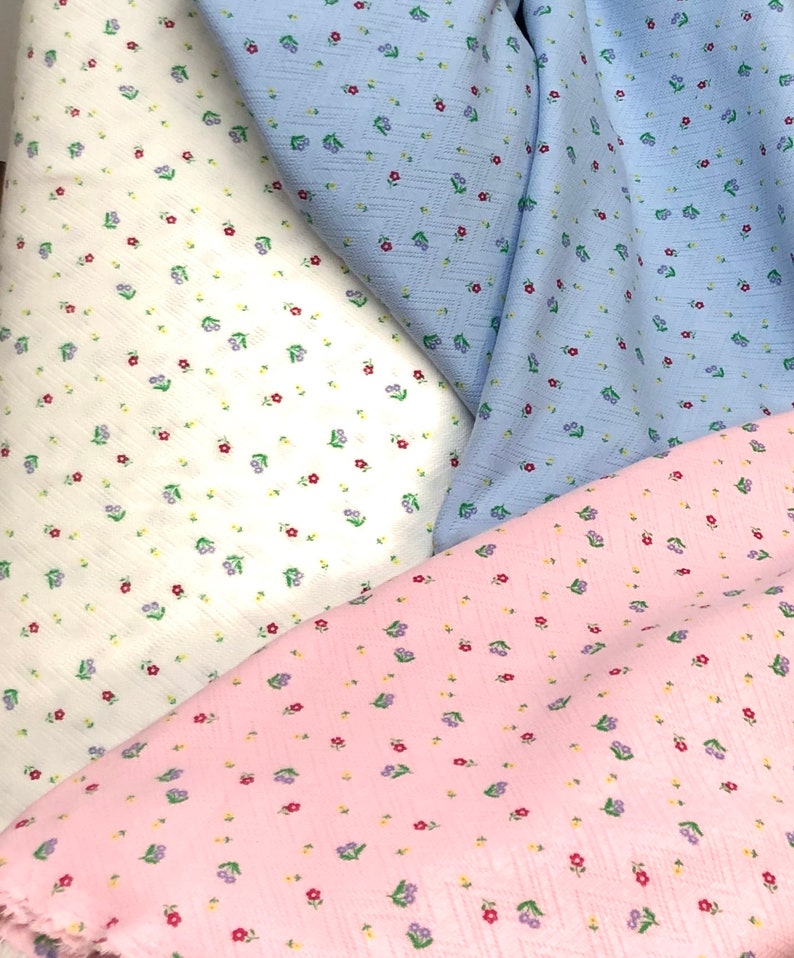 K&ouml;nnte beinhalten: Drei Stoffmuster mit einem kleinen Blumenmuster. Die Muster sind wei&szlig; mit roten Blumen, hellblau mit roten Blumen und rosa mit lila und roten Blumen.
