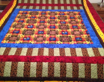 May include: A colorful quilt with a patchwork design featuring a variety of woodland animals and nature scenes. The quilt has a red, brown, green, blue, and yellow color scheme.