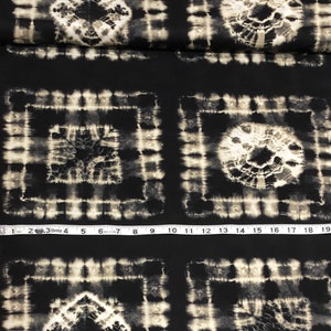 May include: Black fabric with a white tie-dye pattern. The pattern is made up of squares with a circle in the center. The fabric is measured with a tape measure.