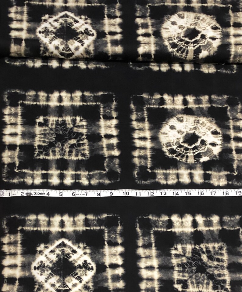 May include: Black fabric with a white tie-dye pattern. The pattern is made up of squares with a circle in the center. The fabric is measured with a tape measure.