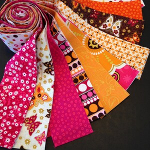 May include: A roll of fabric strips in various shades of pink, orange, and brown with different patterns, including polka dots, butterflies, and paisley designs.