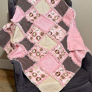 May include: A pink and brown baby quilt with a diamond pattern. The quilt is made of fabric scraps with a bear print and is fringed around the edges.