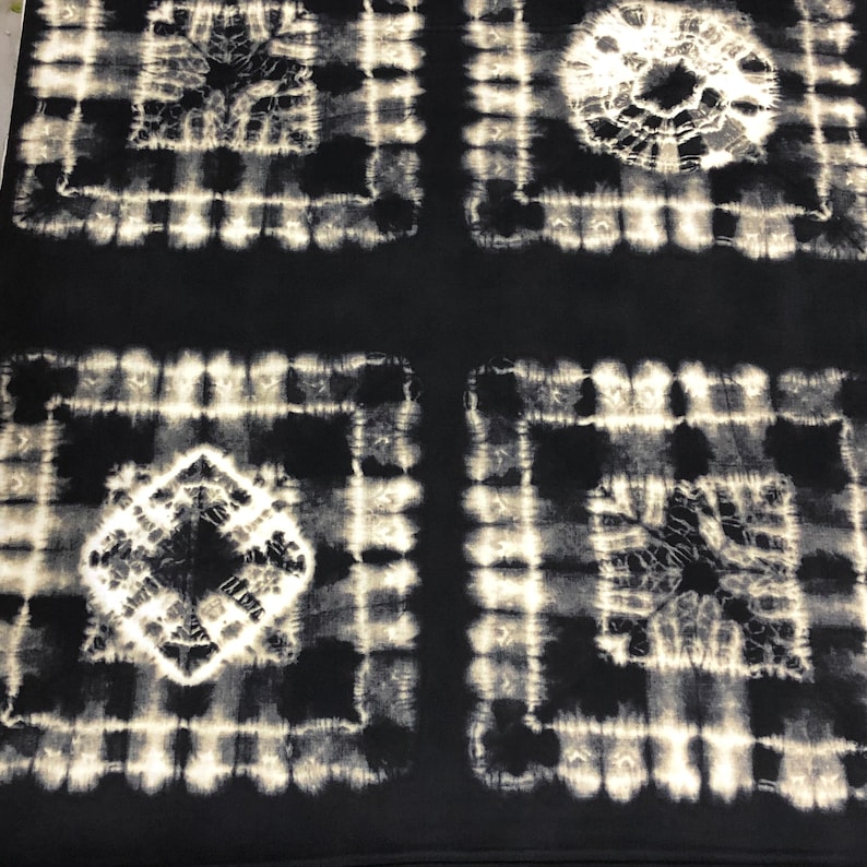 May include: Black and white tie-dye fabric with a repeating pattern of squares. The fabric has a distressed look, with faded areas and a slightly rough texture.