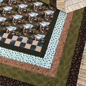Puede incluir: Una colcha con un diseño de patchwork marrón, verde y blanco. El centro de la colcha presenta un patrón repetido de osos marrones en un entorno de bosque. La colcha está bordeada por una serie de rayas en varios tonos de marrón, verde y blanco.