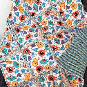 Könnte beinhalten: Eine bunte Babydecke mit einem Monsterdruck auf der einen Seite und blauen und grünen Streifen auf der anderen Seite. Die Decke ist aus weichem, flauschigem Stoff und hat einen ausgefransten Rand.