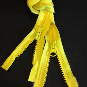 May include: Three yellow zippers with metal sliders. The zippers are knotted together at the top.