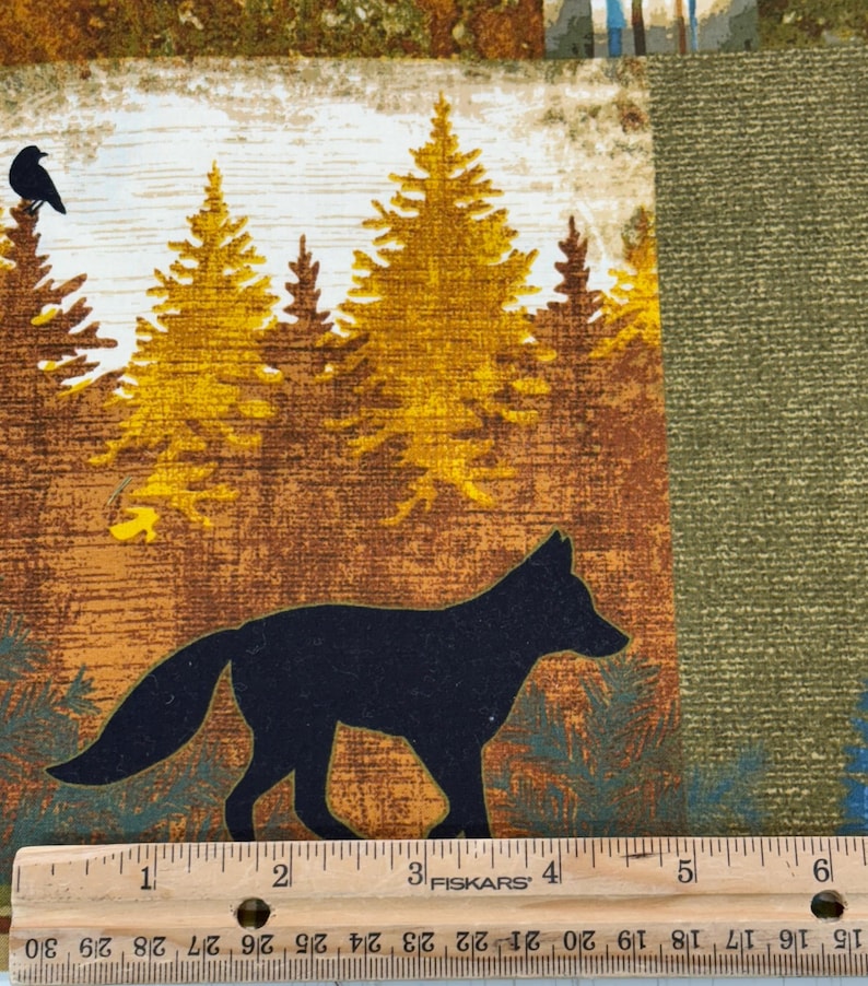 May include: Fabric with a forest scene featuring a black fox silhouette, yellow pine trees, and a black bird. The background has brown, green, and blue tones. A ruler is at the bottom, marked in inches.