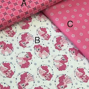 Op de afbeelding: Drie roze en witte stofstalen met verschillende patronen. De bovenste staal heeft een roze en wit geometrisch patroon. De middelste staal heeft een witte achtergrond met een roze pony-patroon. De onderste staal heeft een effen roze achtergrond met een wit stippenpatroon.