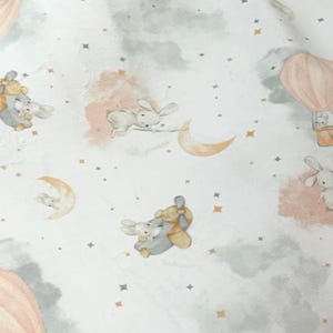 May include: White fabric with a whimsical pattern featuring bunnies, hot air balloons, moons, and stars. The design incorporates soft pink, gray, and gold accents, creating a dreamy, celestial theme. Ideal for nursery decor or baby items.