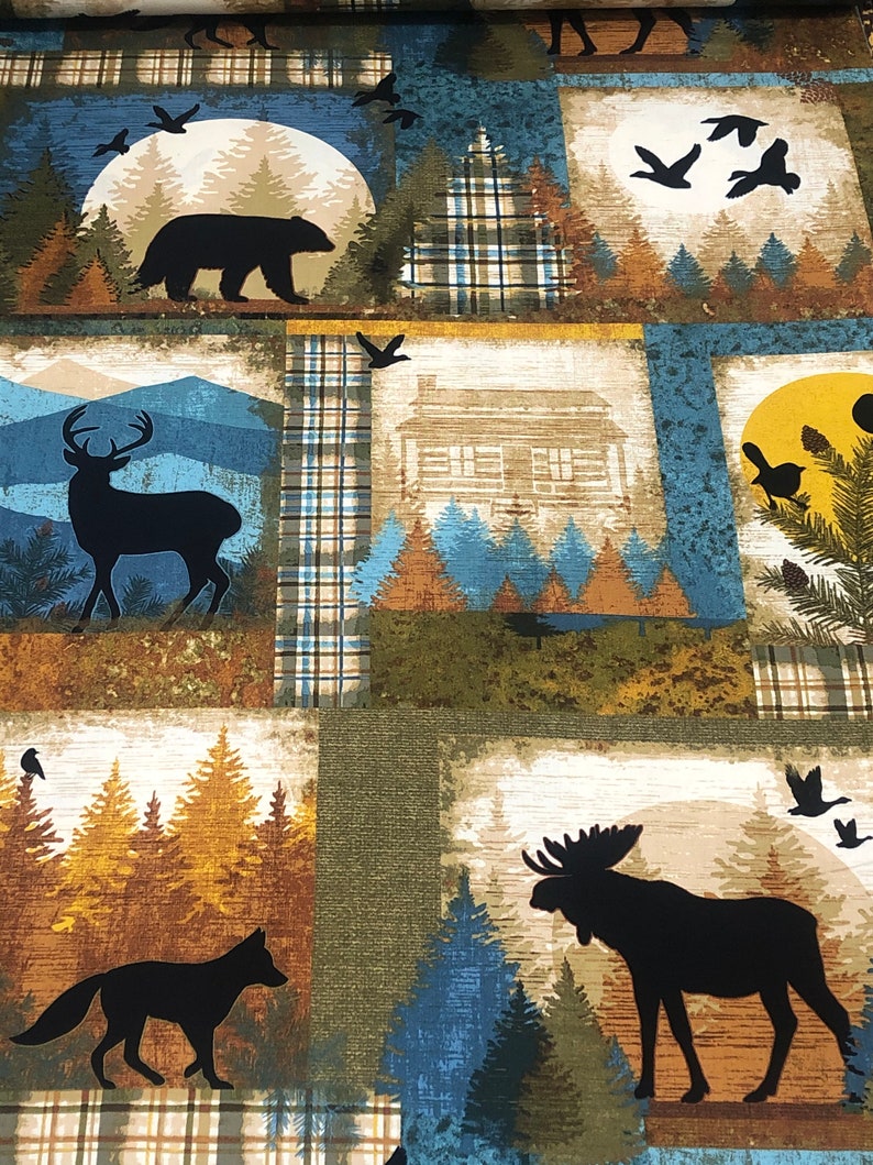 May include: Fabric with a patchwork design featuring woodland scenes. Each square showcases silhouettes of animals like a bear, deer, fox, and moose, set against a backdrop of trees, mountains, and a cabin. The color palette includes shades of blue, brown, and green.