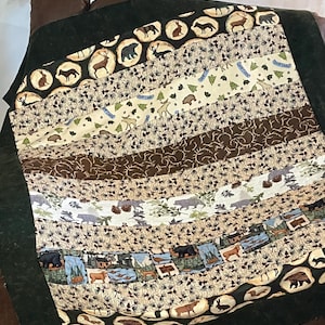 May include: A green and brown patchwork quilt with a woodland theme. The quilt features images of bears, deer, and trees. The quilt is made of various fabrics and has a rustic look.