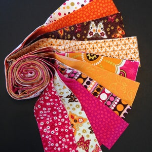 May include: A collection of fabric strips in various shades of orange, pink, and brown with white polka dots, butterfly patterns, and floral designs. The strips are rolled up and fanned out, showcasing the different patterns.
