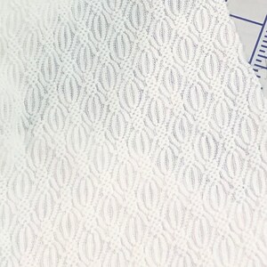 May include: White fabric with a textured pattern of small, repeating ovals. The fabric has a slightly raised, woven texture.