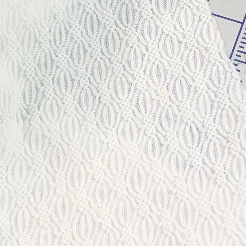 May include: White fabric with a textured pattern of small, repeating ovals. The fabric has a slightly raised, woven texture.